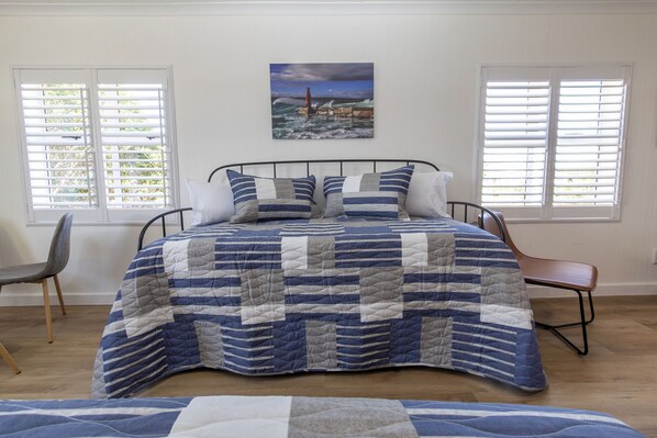 A bedroom with a bed, a chair, a window with blinds, and a painting on the wall.