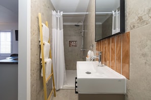 Un baño con un lavamanos blanco, ducha y espejo.