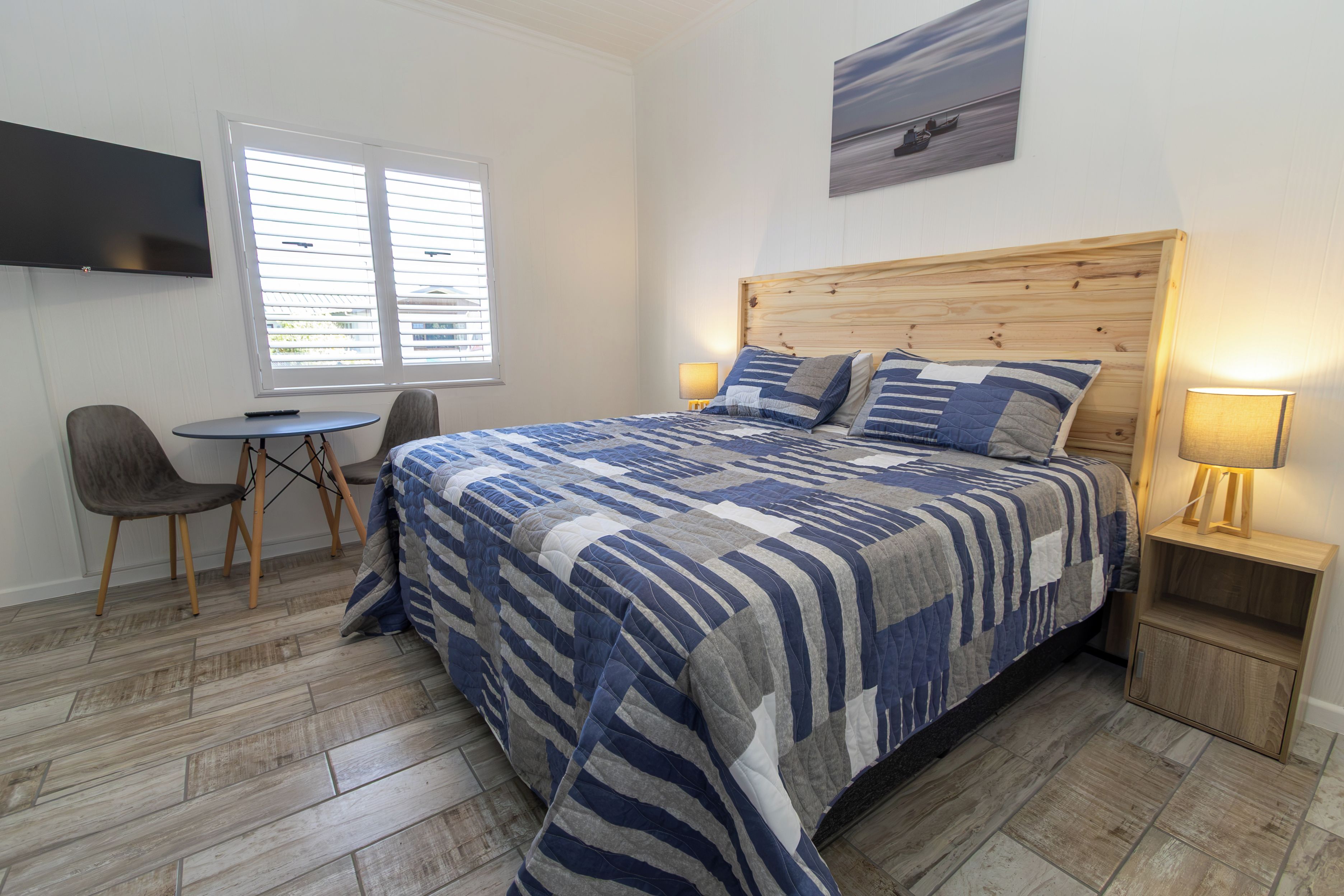 A bedroom with a bed, a desk, a chair, a TV, and a painting on the wall.