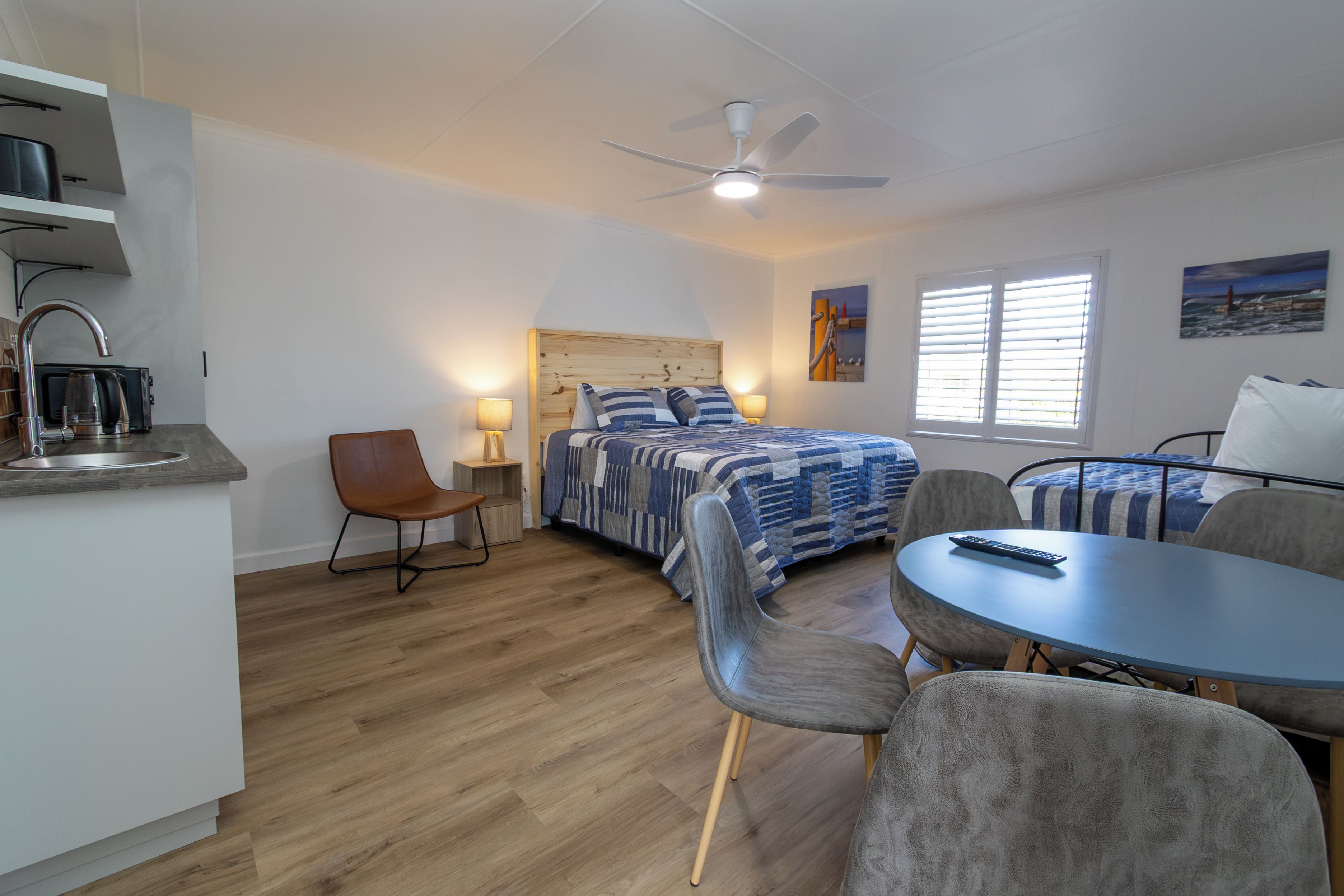 Habitación de hotel compacta con cama, escritorio, silla, mesa, ventilador de techo y ventana.