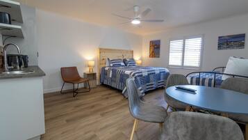 Habitación de hotel compacta con cama, escritorio, silla, mesa, ventilador de techo y ventana.