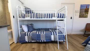 A bunk bed with a quilted bedspread in blue and gray, a white door, and a framed picture on the wall.
