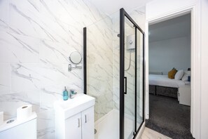 Een moderne badkamer met een douchecabine van glas, een wit wastafeltje en een wand betegeld met marmer.
