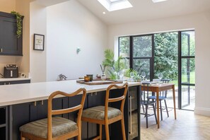 Eine moderne Küche mit einer großen Kochinsel, Barhocker und Blick auf Grün durch große Fenster.