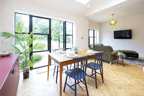 Ein zeitgemäßer Wohnraum mit Essbereich, einer Couch und einem an der Wand montierten Fernseher.