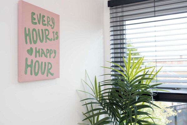 Een muur met een inspirerende quote, een raam met zonwering en een plant in een pot.