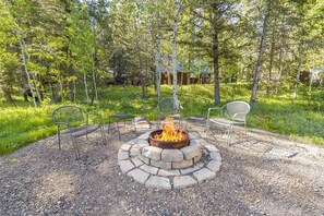 An outdoor seating area with a stone fire pit surrounded by metal chairs. - Peaceful Cabin with Fire Pit & Endless Trail Adventures in Island Park, Idaho (Island Park)