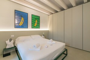 A hotel room with a bed, two nightstands, a wall-mounted light, and two framed pictures of bananas. - Molinella Easy Living Apartment (Modena)