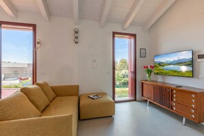 A modern living room with a sofa, a television, and a view of a train outside the window. - Molinella Easy Living Apartment (Modena)