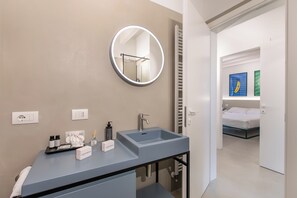 A modern bathroom with a grey sink, a round mirror, and a shower area. - Molinella Easy Living Apartment (Modena)