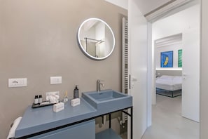 A modern bathroom with a round mirror, a sink, and a toilet. There is a towel on the floor and toiletries on the sink. - La Molinella Garden Suite Apartement (Formigine)