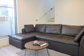 Ein modernes Wohnzimmer mit einem Ecksofa, einem kleinen runden Couchtisch und einer Treppe im Hintergrund.