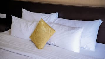 Cama bem arrumada com roupa de cama branca e um único travesseiro dourado.