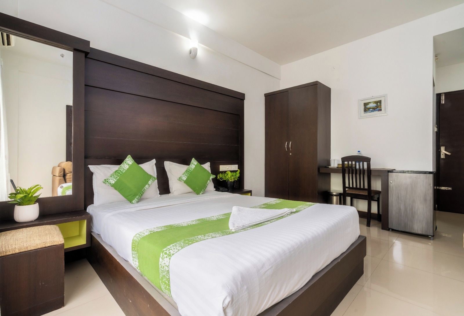 A hotel room with a large bed, a desk, a wardrobe, and a mirror.