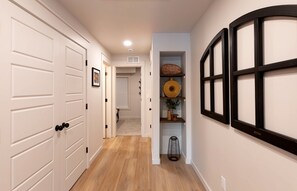 Un couloir avec des portes blanches, un plancher en bois et une étagère ornée d’objets décoratifs.