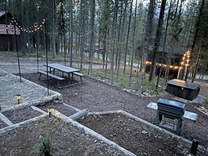 Un espace extérieur rustique agrémenté d’un banc en bois, d’un foyer et de guirlandes lumineuses.