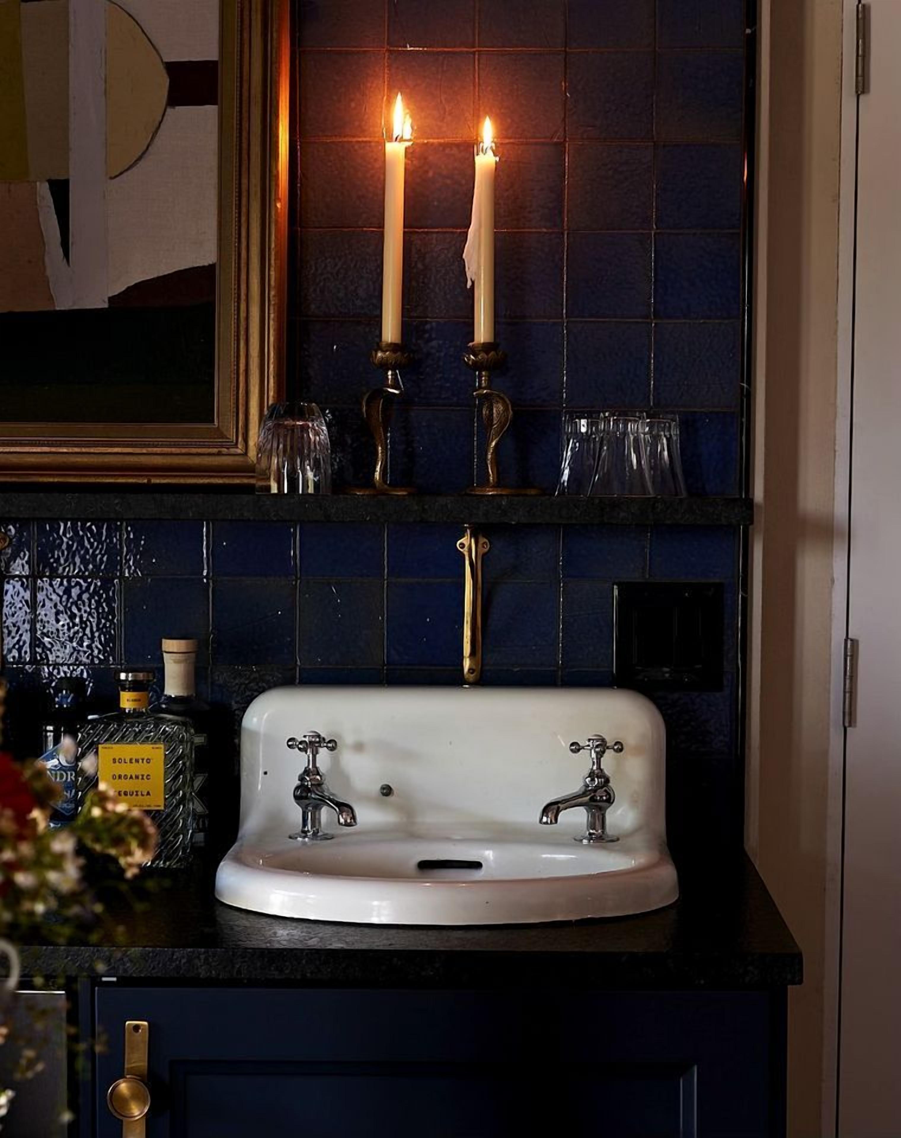 Un bagno con un lavandino bianco, due candele accese e uno specchio sopra il lavandino.