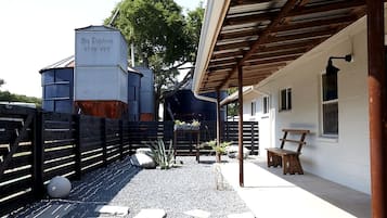 Un área al aire libre techada con estructura metálica identificada como 'Big Puchman STOR VEE', un banco de madera y un edificio blanco con ventanas.