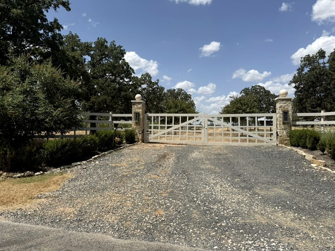 A gated driveway leading to a building with a stone pillar and a spherical finial on top.