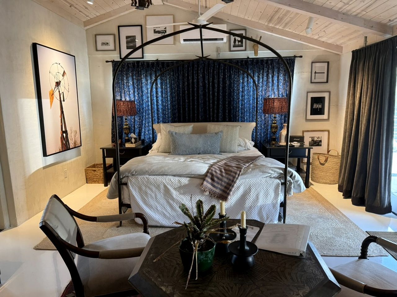 Une chambre à coucher comprenant un lit, des tables de chevet, une chaise, une table avec une plante et un ventilateur de plafond.