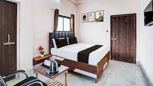 Quarto de hotel com cama, escrivaninha, cadeira, televisão e janela com cortinas.