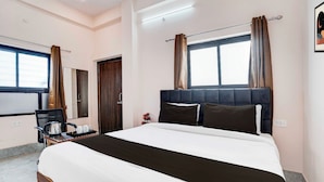 Quarto de hotel com cama, escrivaninha, cadeira e janela com cortinas.