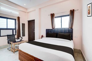 A hotel room with a large bed, a wooden side table, a chair, and a window with curtains. - Townhouse Prayag Central Junction (Prayagraj)