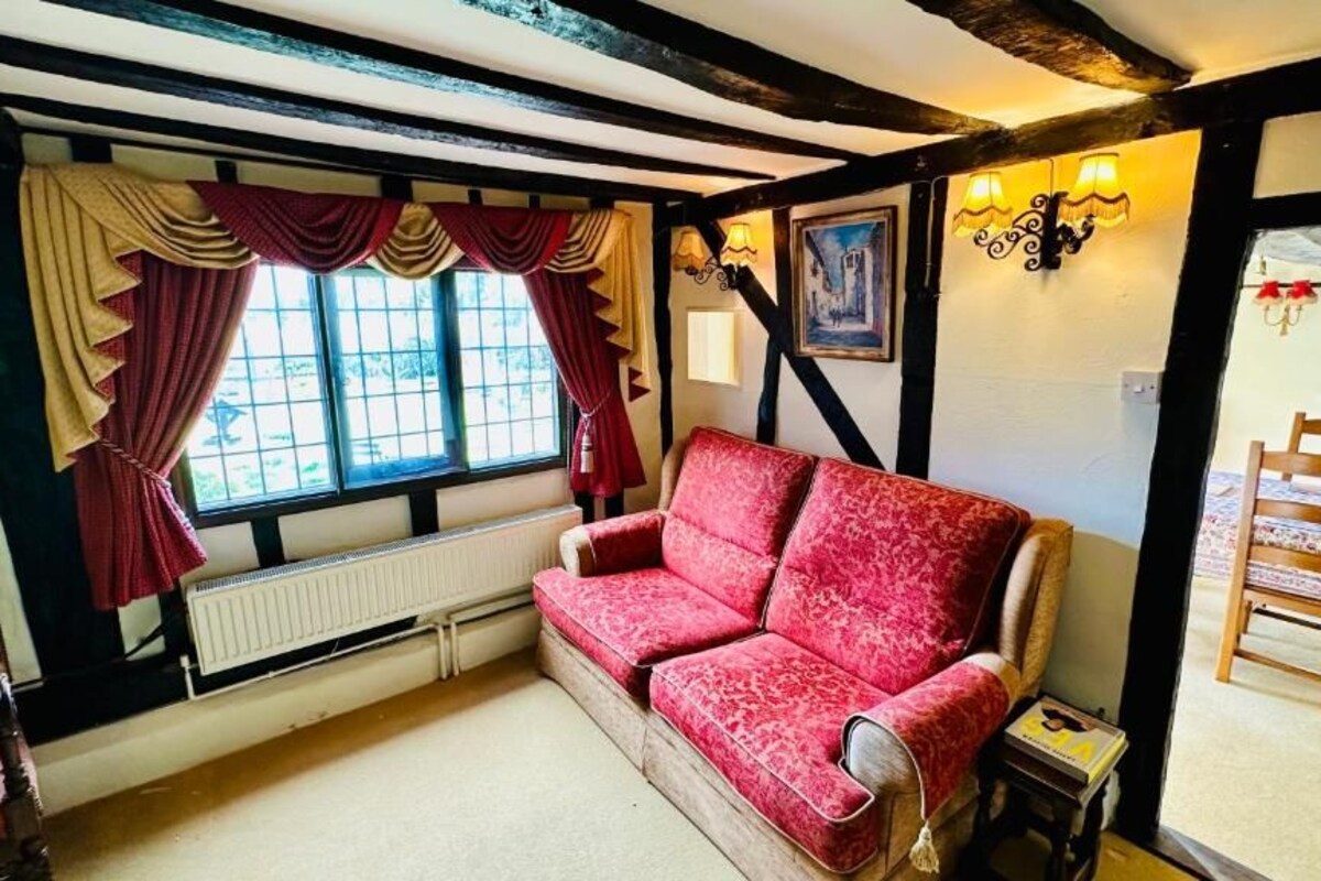 Quarto com sofá vermelho, cadeira de madeira, radiador e janela com cortinas.