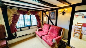 Quarto com sofá vermelho, cadeira de madeira, radiador e janela com cortinas.