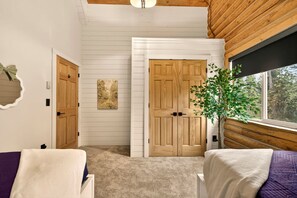 A room with a wooden ceiling, a large window with a view of trees, a door with a mirror, and a plant by the window. - Serene Mountain Lodge with Fireplace & Wildlife Views in Island Park, Idaho (Island Park)