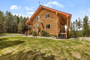 A log cabin with a porch, a satellite dish, and a staircase leading to the entrance. - Serene Mountain Lodge with Fireplace & Wildlife Views in Island Park, Idaho (Island Park)