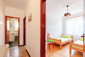 A room with two wooden beds, a chair, a small table, a wooden floor, a mirror, a picture on the wall, and a window with curtains. - A1 - Apartment 50m from the beach, with the sea view (Korčula)