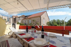 An outdoor dining area with a table set for two, a wine bottle, and a view of a stone building with a red roof. - A1 - Apartment 50m from the beach, with the sea view (Korčula)