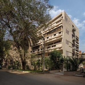 A multi-story building with balconies, surrounded by trees and a clear sky.