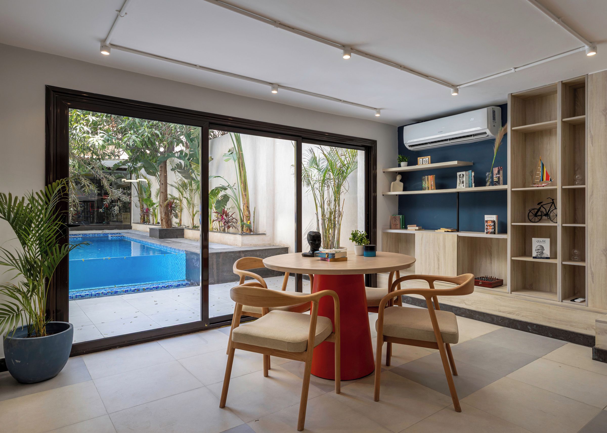 Un salon moderne avec vue sur la piscine, une table ronde avec des chaises et une bibliothèque.