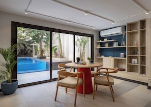 A modern living room with a pool view, a round table with chairs, and a bookshelf.