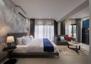 A modern hotel room with a large bed, a sofa, a coffee table, and a view of the outdoors.