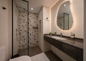 A modern bathroom with a glass-enclosed shower, a large mirror, and a marble countertop.