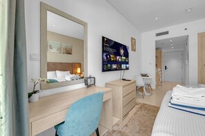 A modern hotel room with a large bed, a desk, a chair, a TV, and a bathroom visible in the background. - Luxury Studio on the Palm | Beach & Rooftop Pool (Dubai)