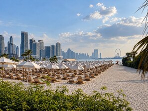 A beach with rows of sun loungers and umbrellas, a city skyline in the background, and a Ferris wheel. - Luxury Studio on the Palm | Beach & Rooftop Pool (Dubai)