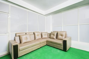 Un sofá seccional color beige con almohadones acolchados en una habitación con paredes blancas y una alfombra verde.