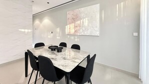 A modern conference room with a marble table, black chairs, recessed ceiling lighting, and a large abstract painting on the wall.