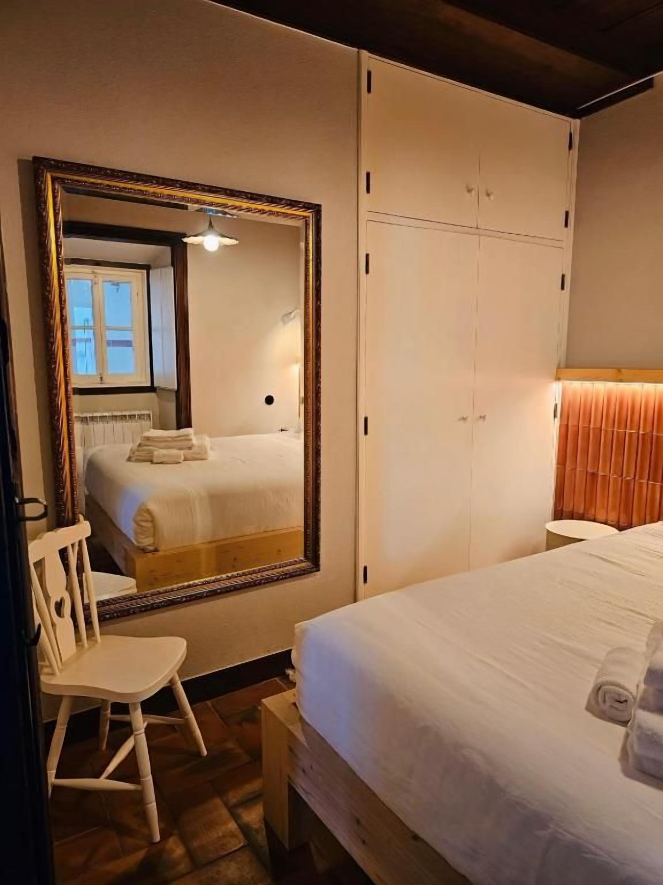 Quarto de hotel com cama, cadeira, guarda-roupa e um espelho grande.