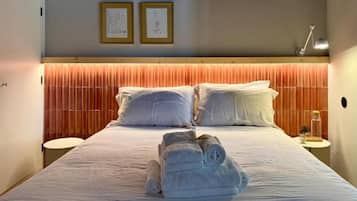 A hotel room with a bed, two framed pictures on the wall, a bedside lamp, and a rolled towel on the bed.