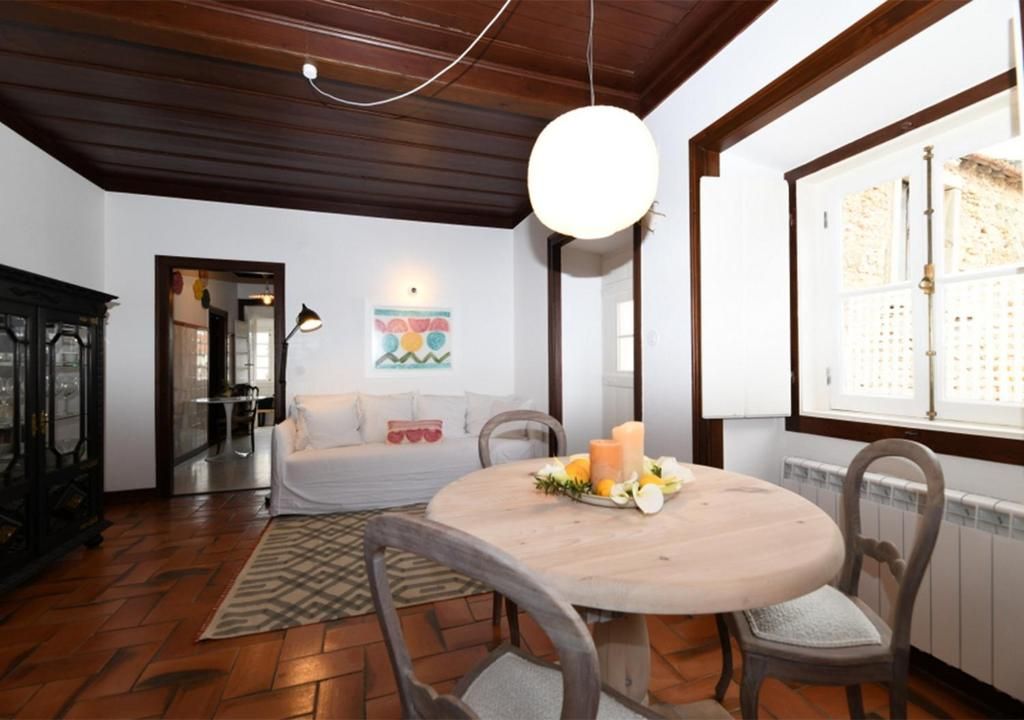 A dining area with a round table, chairs, a hanging light, and a window with a view.