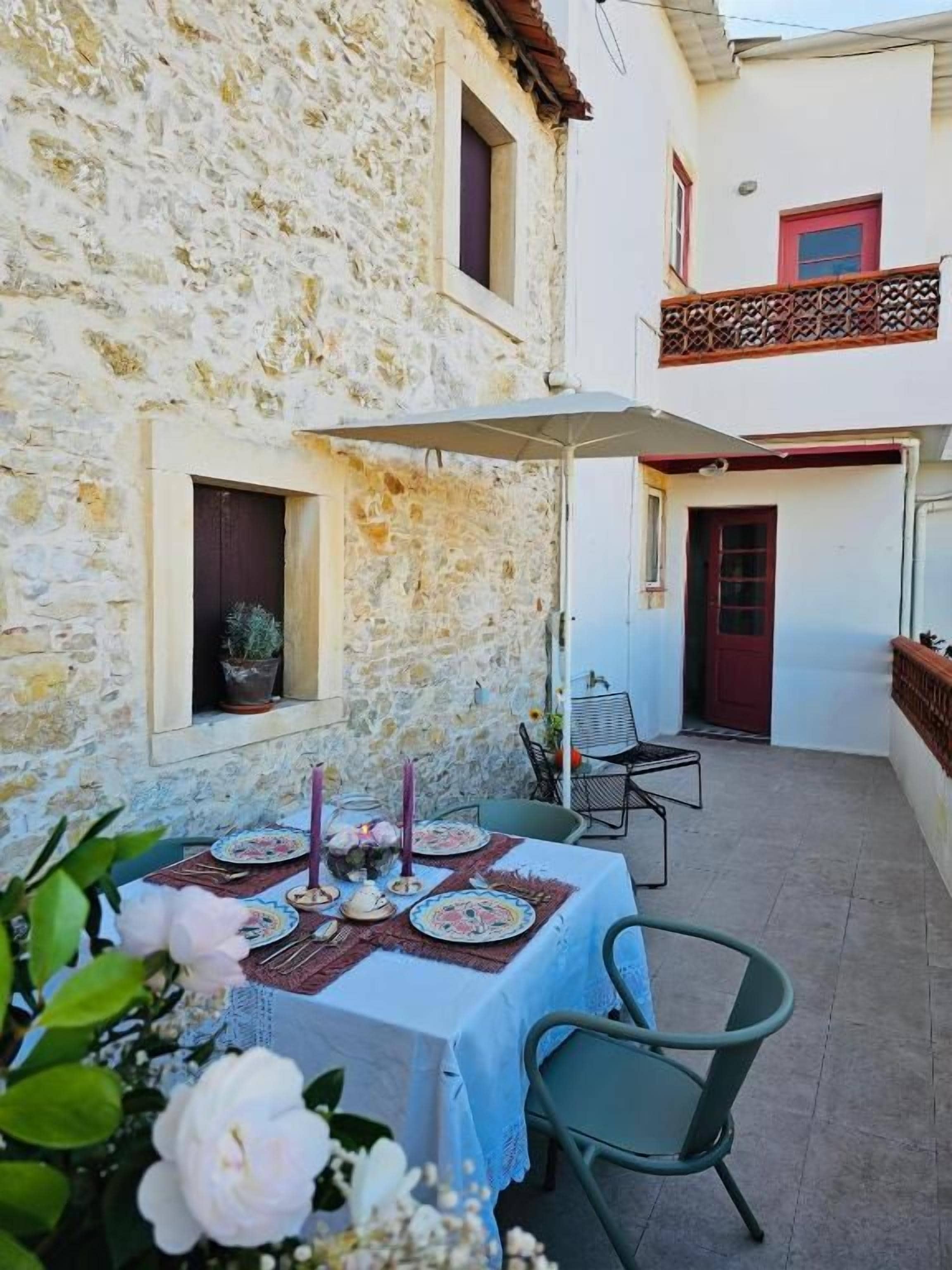 A stone building with a dining area set up outside, featuring a table with plates, candles, and flowers.