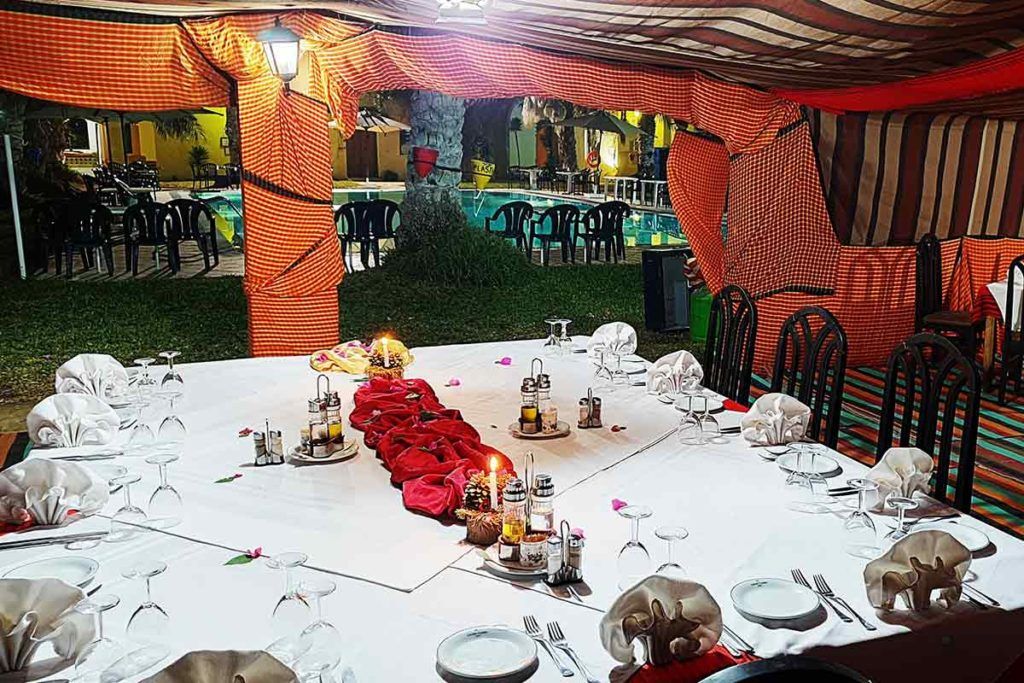 An outdoor dining area with tables set for a meal, surrounded by chairs and a pool in the background.