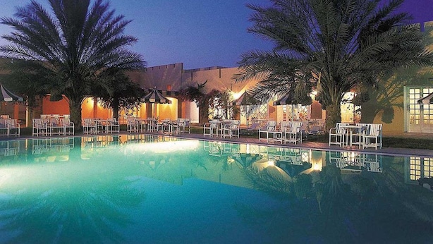 A pool area with lounge chairs and palm trees, surrounded by buildings with warm lighting. - Sun Palm  (douz)