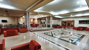 A spacious lobby with red seating, a central decorative fountain, and a patterned floor. - Sun Palm  (douz)