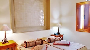 A bedroom with two beds, each with a pillow and a lamp. There is a window with blinds and a wooden door. - Sun Palm  (douz)